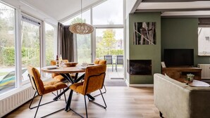 Een moderne woonkamer met een eethoek, grote ramen en een open haard.