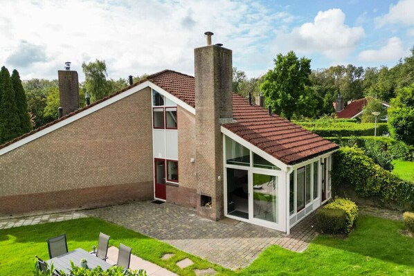 Ein modernes Haus mit Backsteinfassade, einem Wintergarten und einem gepflegten Garten.