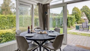 A dining area with a round table set for four, large windows, and a view of a garden.