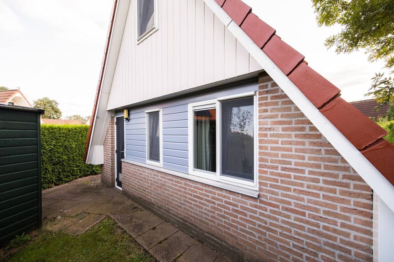 Ein Haus mit geneigtem Dach, Ziegelaußenwand und drei Fenstern mit weißen Rahmen.