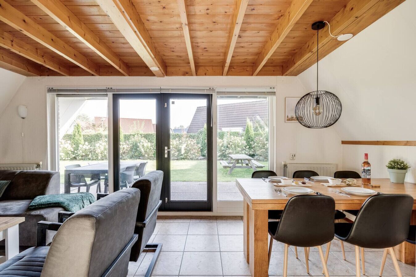 A modern kitchen with a wooden ceiling, a dining area with a table and chairs, and a sliding glass door leading to a garden.