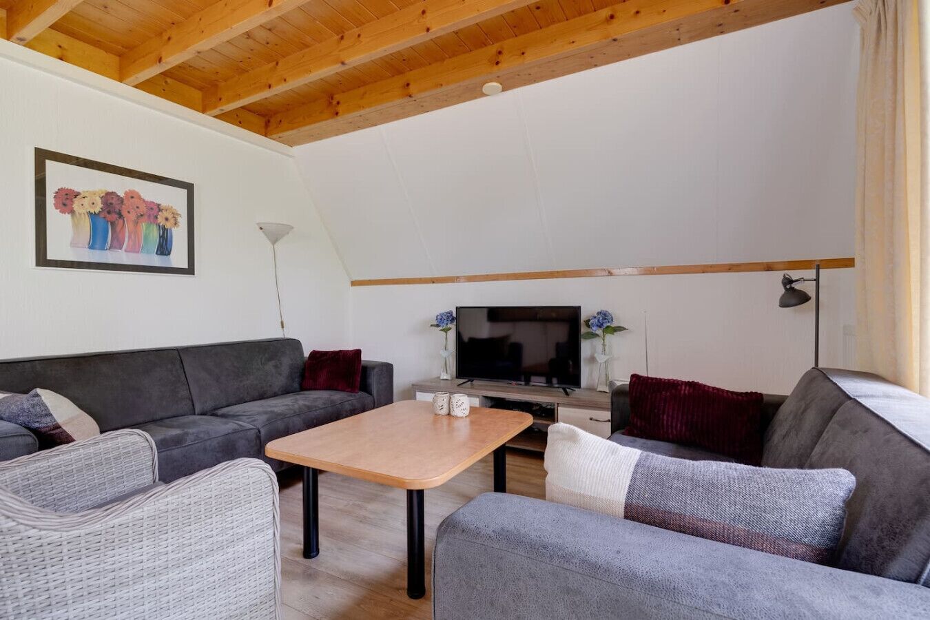 A modern living room with a wooden ceiling, grey sofas, a wooden coffee table, and a flat-screen TV.