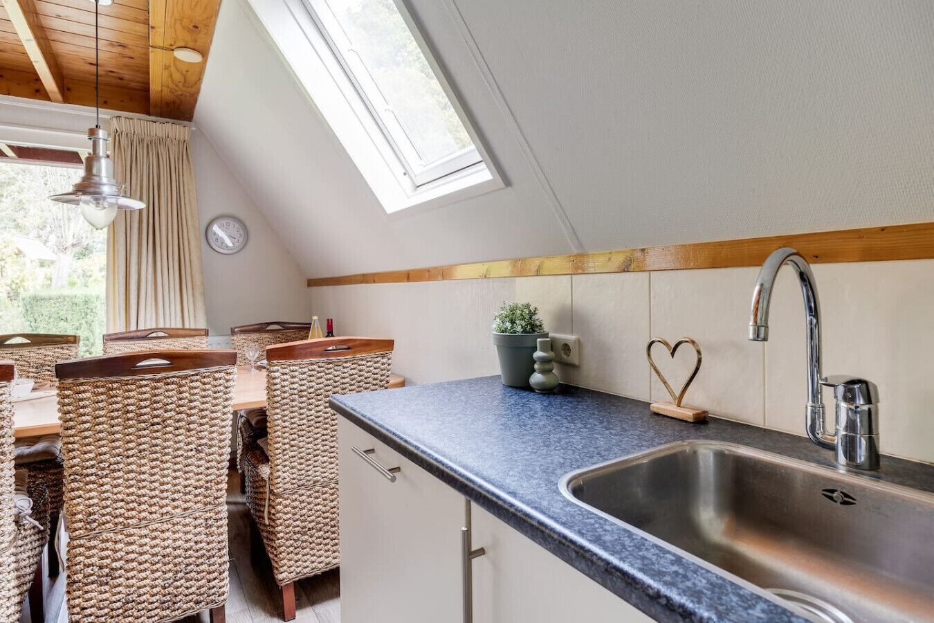 A kitchen with a sink, wooden chairs, a potted plant, and a heart-shaped soap holder.