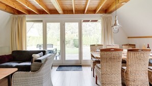 A cozy room with a wooden ceiling, a sofa, wicker chairs, a dining table, and a view through large glass doors. - Meadow Pipit I Detached Chalet with Broad Garden (Zwiggelte)