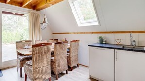 A cozy kitchen with wooden beams, a dining area with woven chairs, a small sink, and a clock on the wall. - Meadow Pipit I Detached Chalet with Broad Garden (Zwiggelte)