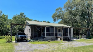 A rustic cabin with a porch, a car parked in front, and a grassy yard. - Beautiful brick home w/ large porch and 3 bedrooms (Bowman)