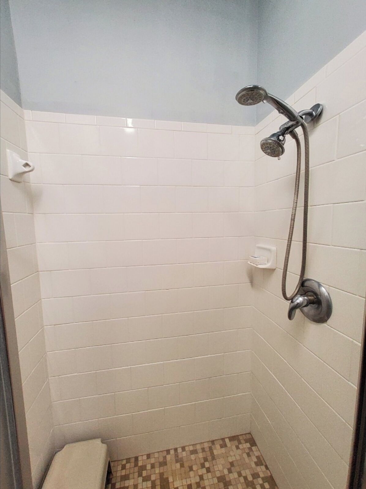 A small, tiled shower room with a showerhead and hose.