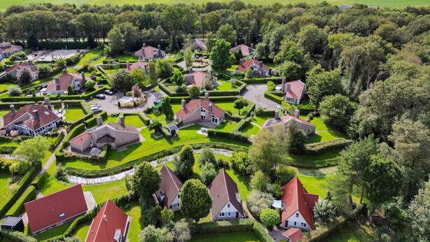 An aerial view of a residential area with houses arranged in a semi-circular pattern around a central green space, surrounded by fields and trees.