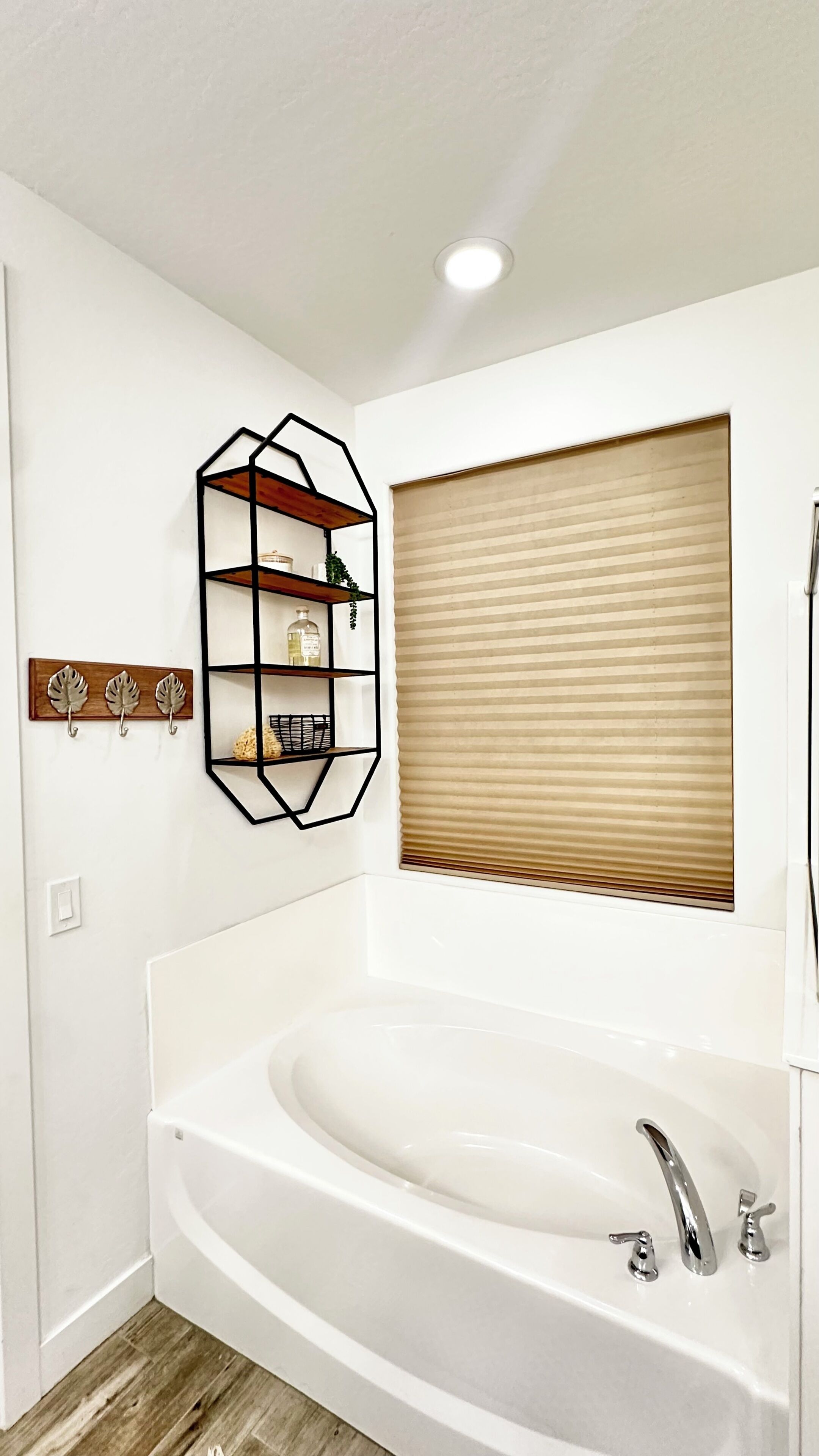 Une salle de bain moderne avec une baignoire sur pieds, une étagère au design géométrique et une fenêtre avec des stores.