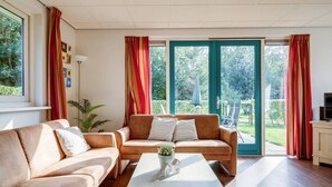 A living room with a beige sofa, a coffee table, and a view of a garden through large glass doors. - Pheasant I Beautiful Quiet Holiday Home with Garden (Zwiggelte)