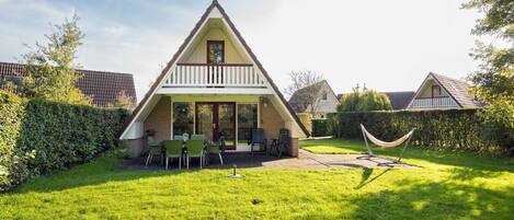 A triangular-roofed house with a patio, green lawn, and a hammock.