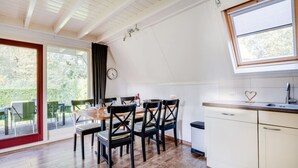 Une cuisine avec un coin repas, un plancher en bois, des armoires blanches et une fenêtre donnant sur un espace verdoyant.
