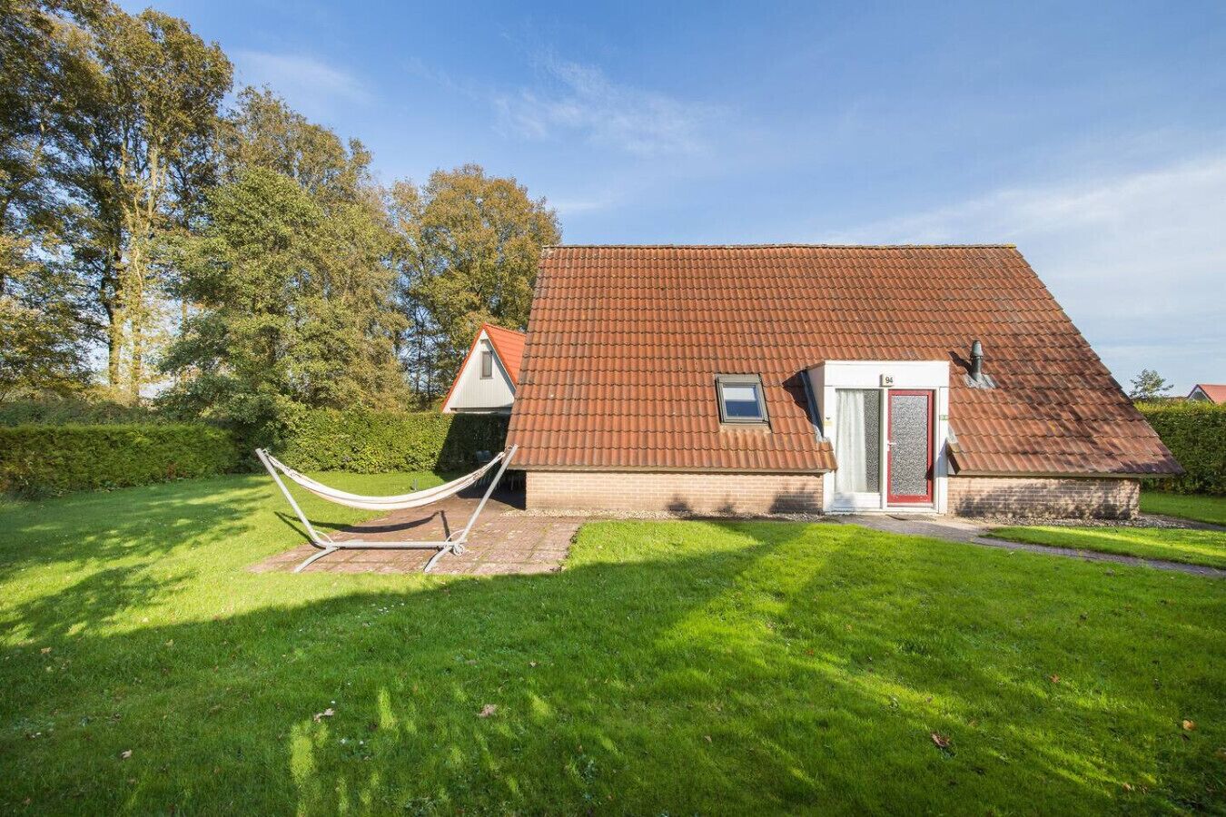Een huis met een rood pannendak, een kleine garage en een hangmat in de voortuin.