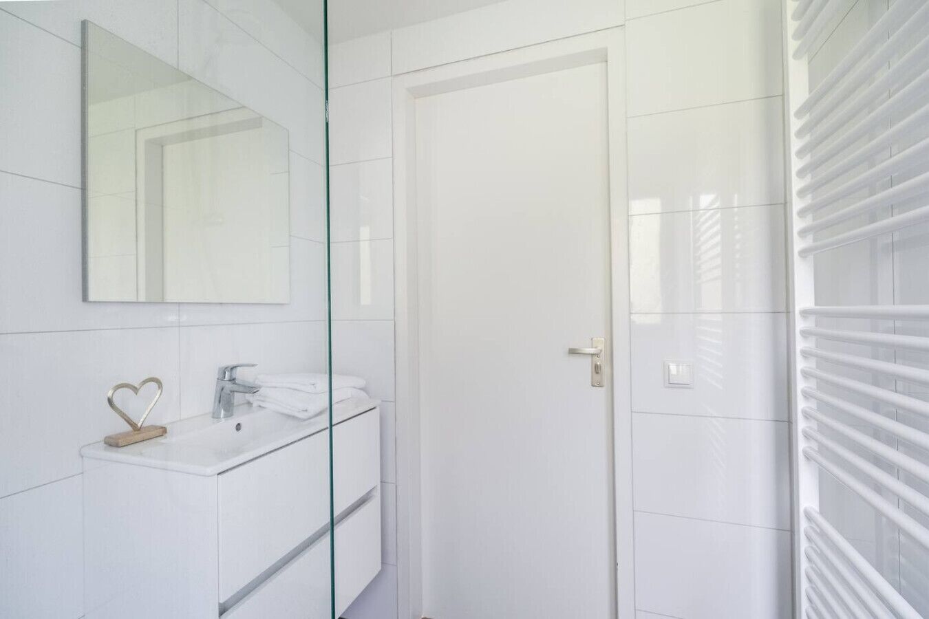 A modern bathroom with a glass shower enclosure, a white sink with a heart-shaped soap holder, and a large mirror.
