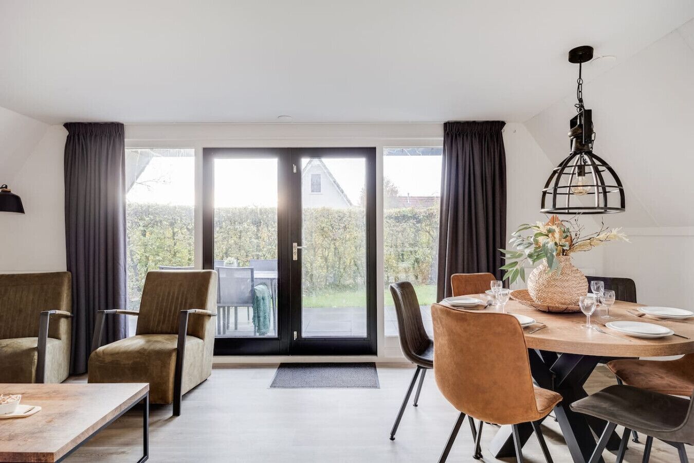 Un coin repas avec une table ronde dressée pour quatre personnes, entourée de chaises, et une vue sur un jardin par une porte vitrée.