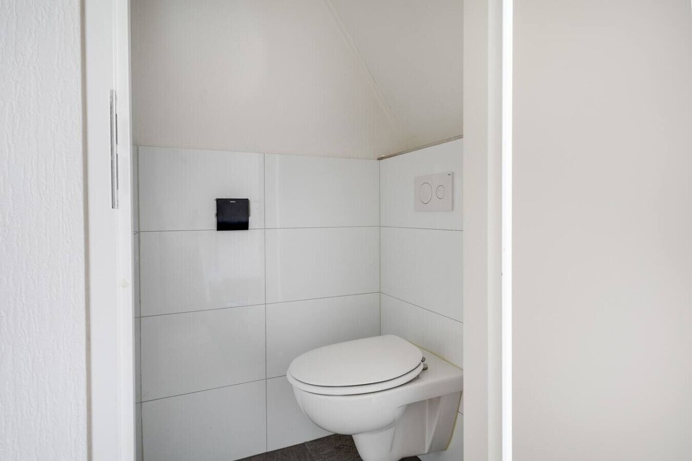 Un baño pequeño y blanco con inodoro, dispensador de toallas y un interruptor de luz en la pared.