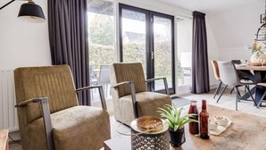 Una sala de estar moderna con dos sillones cómodos, una mesa de comedor con una planta y una botella, y un ventanal con cortinas.