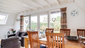 A dining area with wooden chairs and a table, large windows with curtains, and a heart-shaped decoration on the wall. - Tufted Duck I Vacation Home with Modern Interior (Zwiggelte)