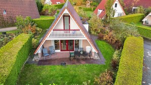 A triangular house with a red roof, a balcony, and a patio area with outdoor furniture. - Tufted Duck I Vacation Home with Modern Interior (Zwiggelte)