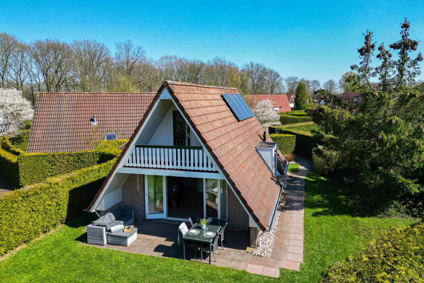 Una casa de dues plantes amb teulada inclinada, un balcó i una zona de pati amb mobles d'exterior.