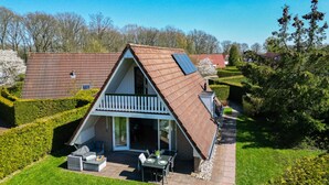 Une maison à deux étages, dotée d’un toit en pente, d’un balcon et d’un patio aménagé avec du mobilier d’extérieur.