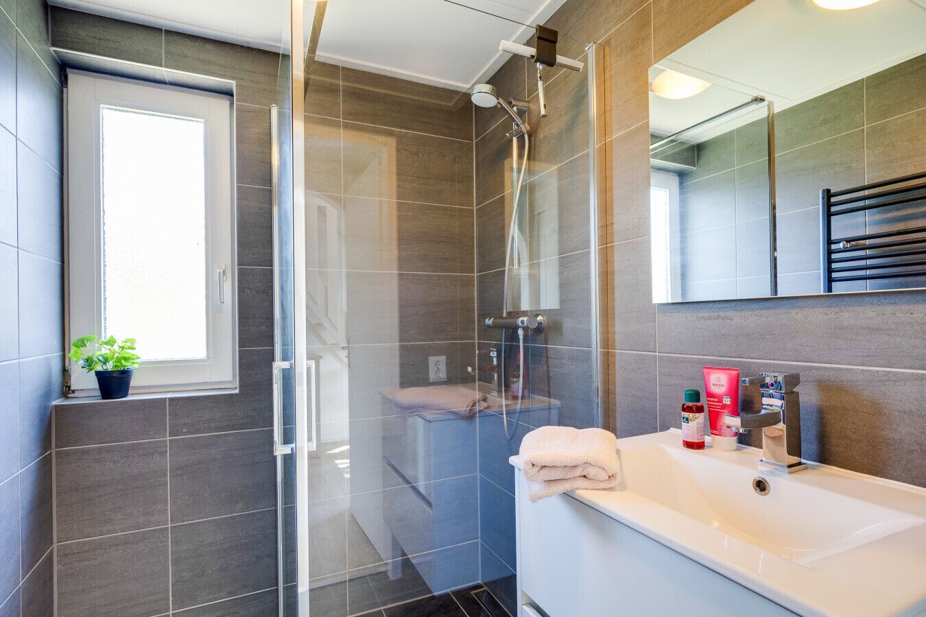 Une salle de bain moderne avec une douche à parois de verre, un lavabo blanc et un miroir au-dessus.