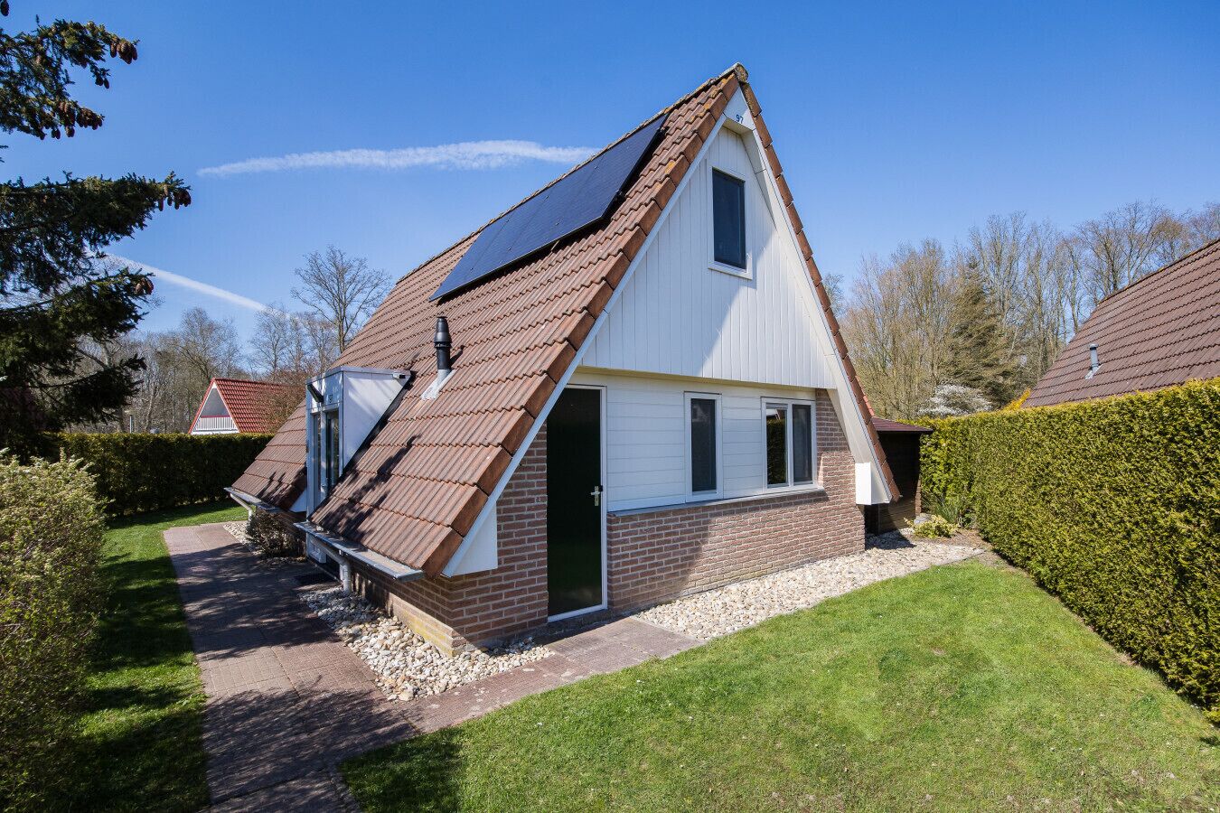 A single-story house with a sloped roof, solar panels, and a brick foundation.