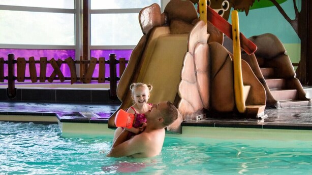A swimming pool with a slide and a child being held by an adult. - Dunnock I Home with Fireplace in Surrounding Garden (Zwiggelte)