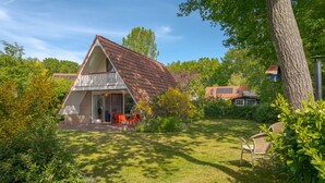 A house with a sloped roof, a balcony, and a garden with a lawn and trees. - Dunnock I Home with Fireplace in Surrounding Garden (Zwiggelte)