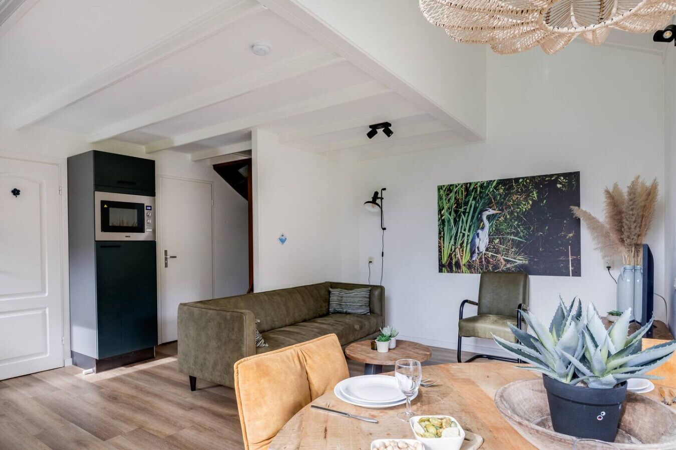 A modern living room with a sofa, dining table, and chairs. There is a painting on the wall and a potted plant on the table.