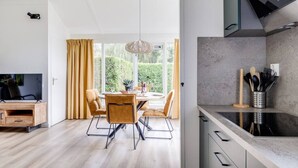 A modern kitchen with a built-in stove, a dining area with a round table and four chairs, and a large window with curtains. - Blue Heron I Modern Home with Fine Garden (Zwiggelte)