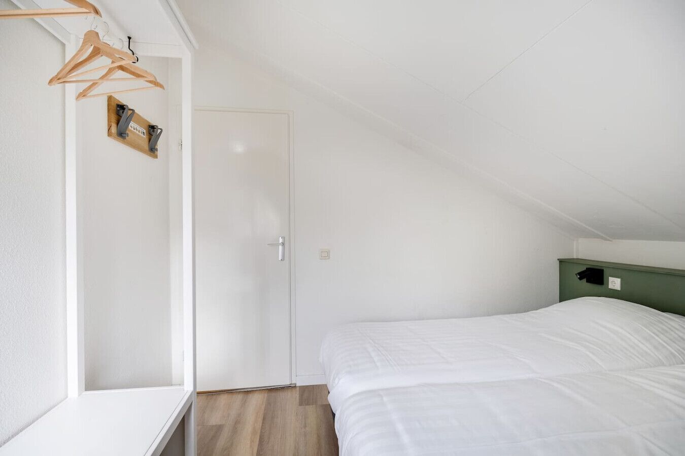 Un dormitorio con una cama blanca, cabecera verde y un armario de madera con perchas.