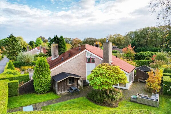 A house with a red roof, a brick chimney, and a garden with a bench and a small shed. - Red Kite I Stylish Bungalow with Private Garden (Zwiggelte)