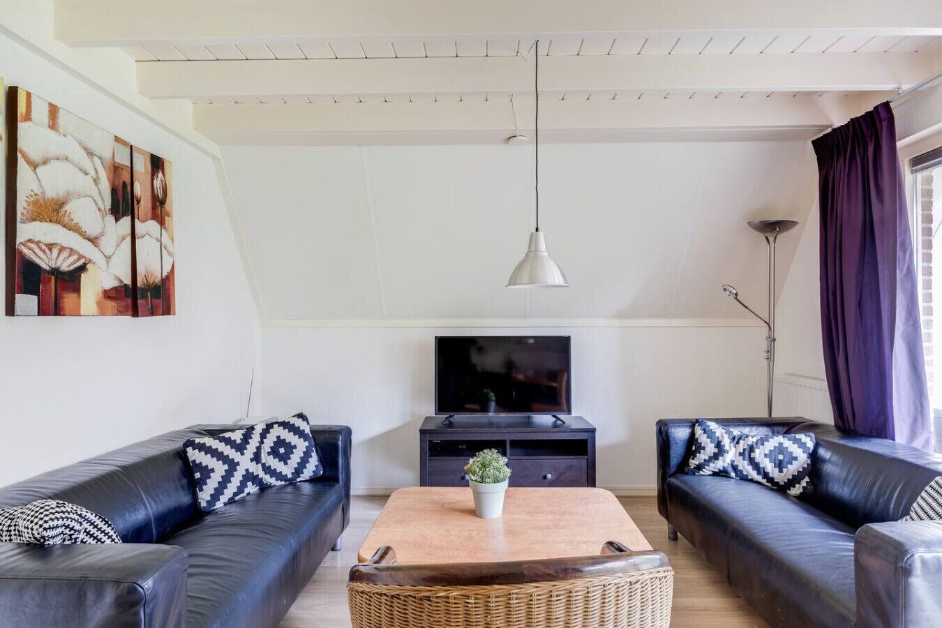 A modern living room with two black leather sofas, a wooden coffee table, and a flat-screen TV on a dark wooden stand.