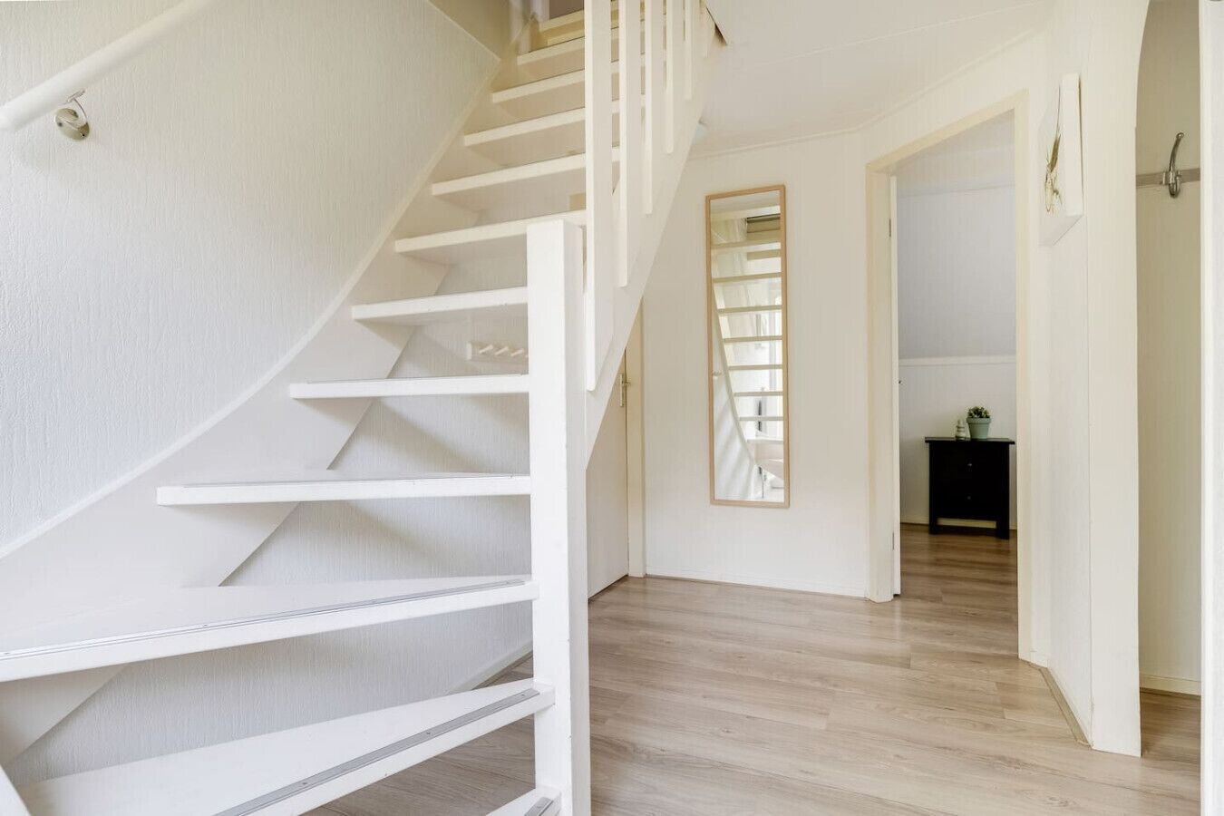 Eine Wendeltreppe mit weißen Geländern führt zu einem Raum mit Holzboden und einem schwarzen Beistelltisch mit einer Pflanze.
