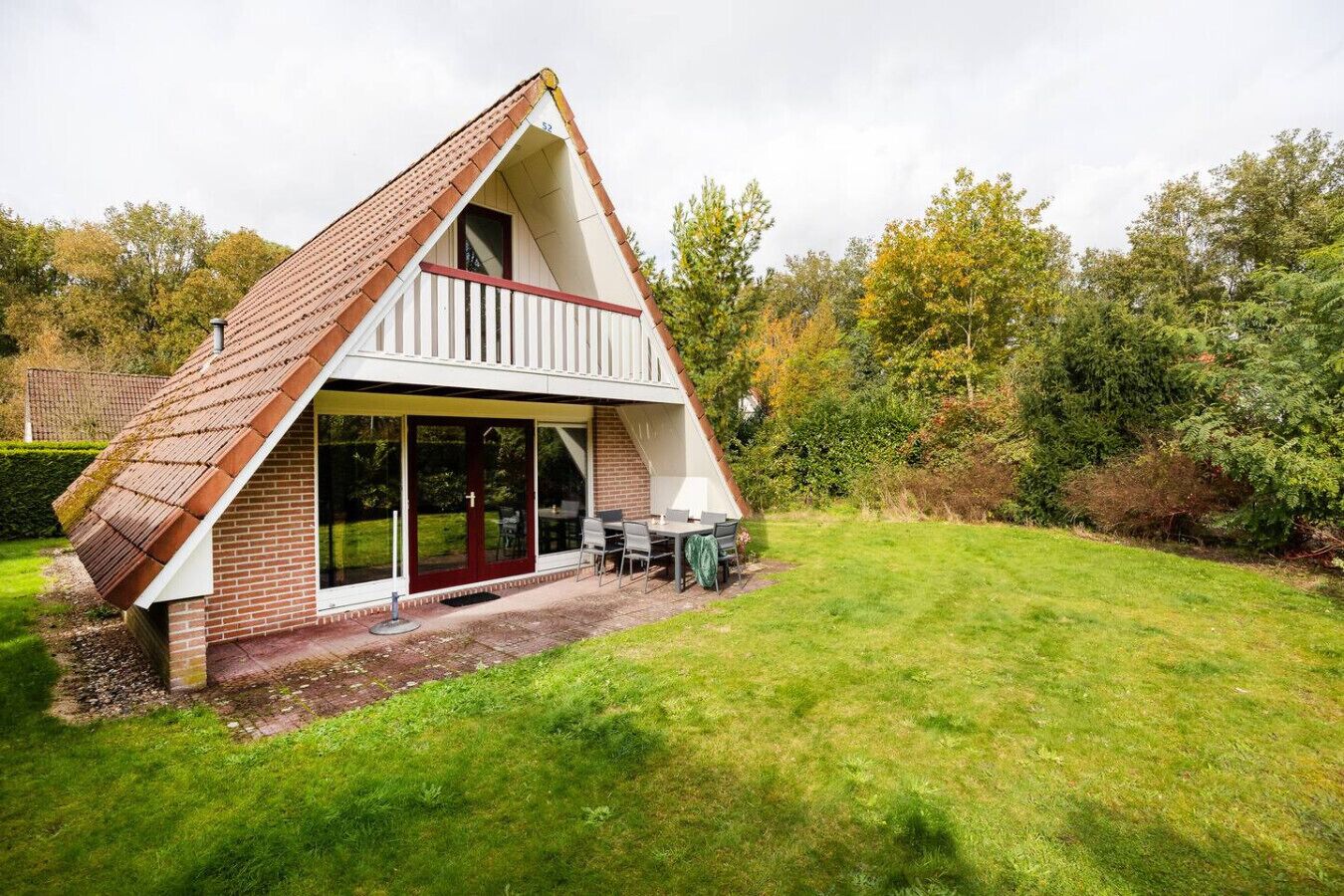 A small, triangular house with a sloped roof, a balcony, and a patio area with outdoor furniture.
