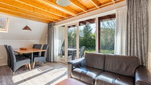 Un espacio acogedor con techo de madera, un sofá de cuero, una mesa de comedor con sillas y un amplio ventanal corredero que da a un patio exterior.