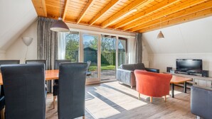 Una sala de estar moderna con techo de madera, un comedor con sillas negras, un sofá rojo y un televisor.