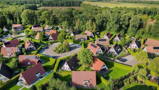 A residential area with houses arranged in a grid pattern, surrounded by green fields and trees.