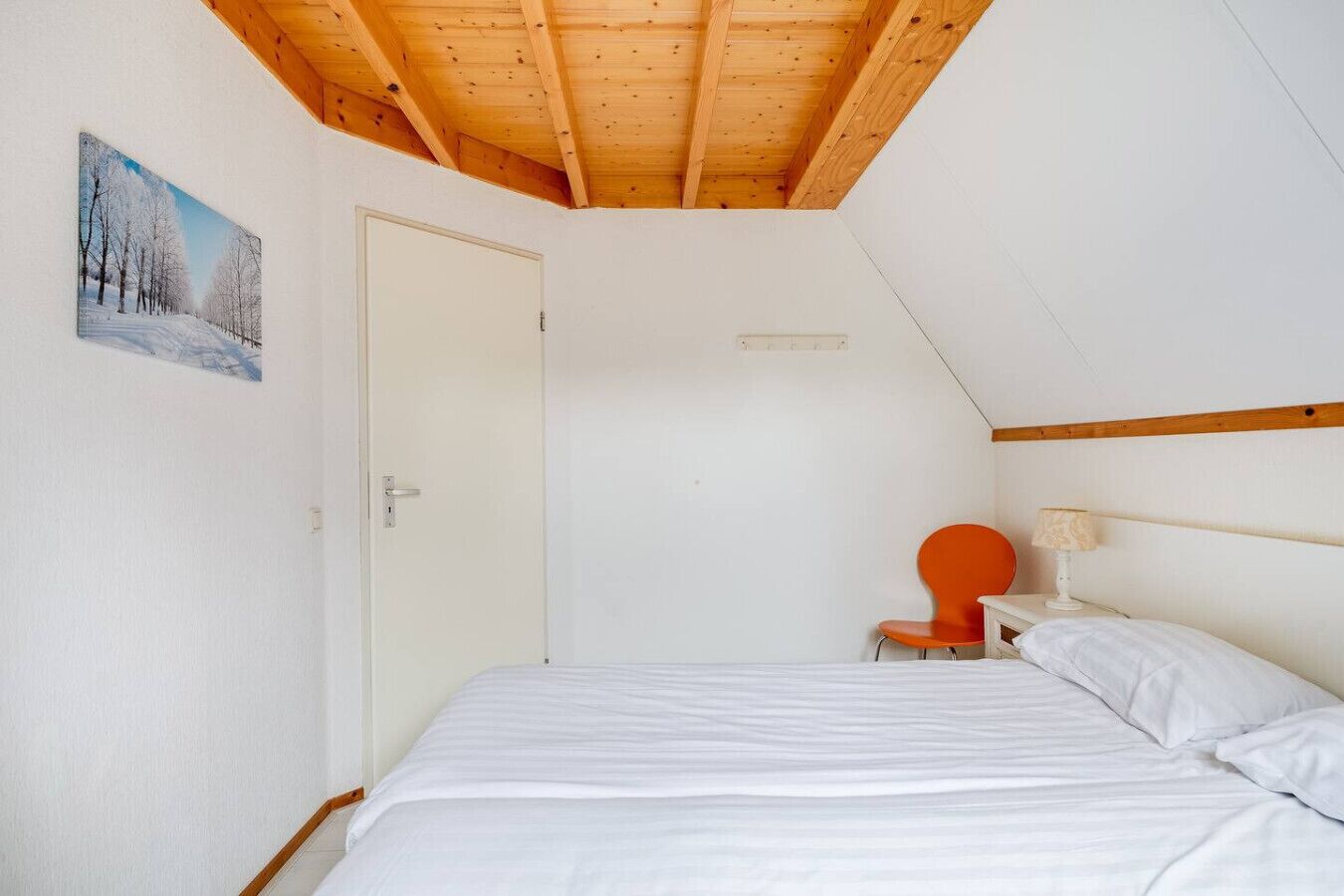 Une chambre avec un plafond en pente, un lit, une chaise et une table de chevet.