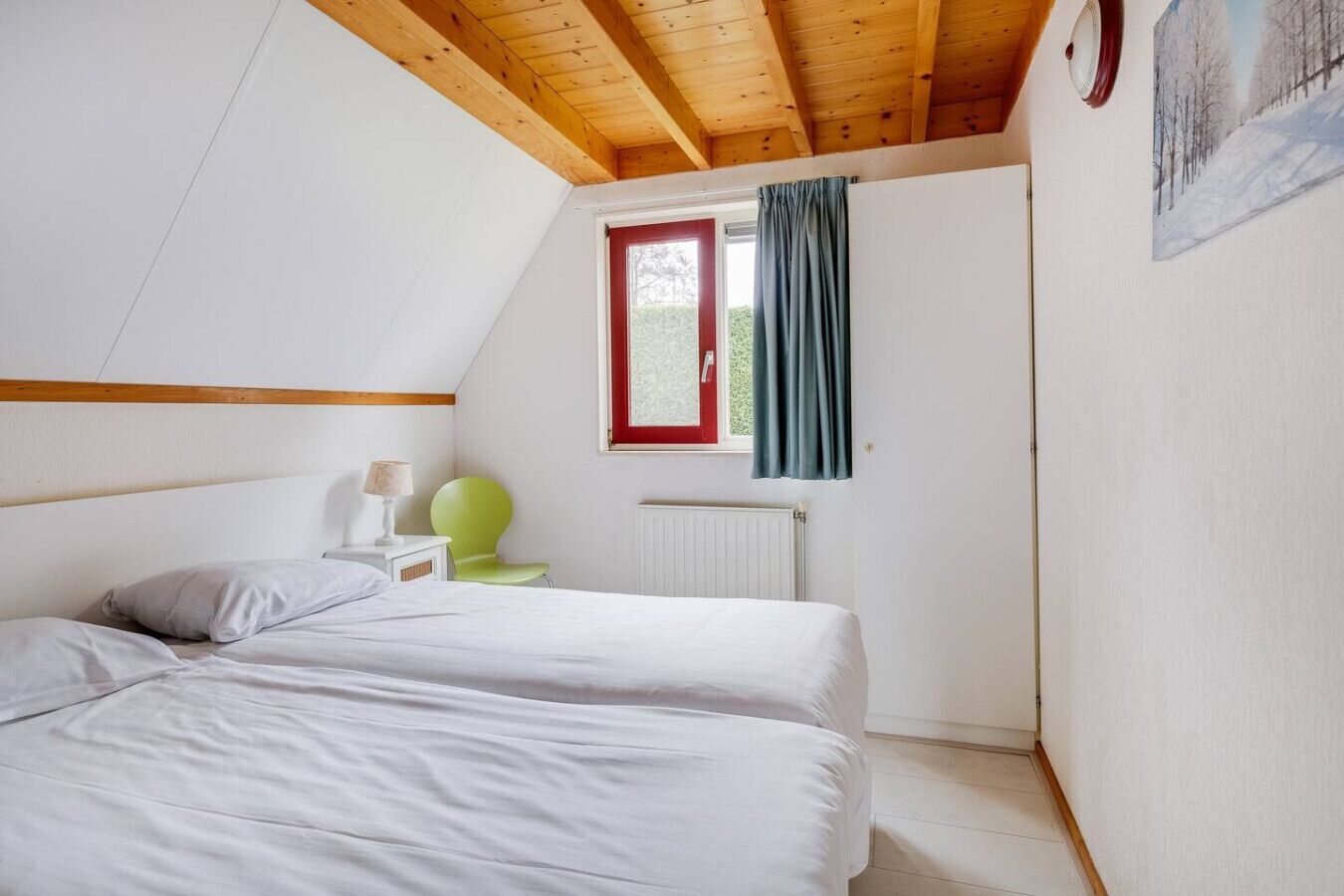 A bedroom with two beds, a window with curtains, a radiator, and a green chair.