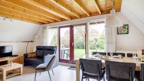 A modern living room with a wooden ceiling, a sofa, a TV, and a dining area with chairs and a table.