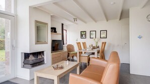 Een moderne woonkamer met een open haard, een eethoek met een tafel en stoelen, en een groot raam dat voor natuurlijk licht zorgt.