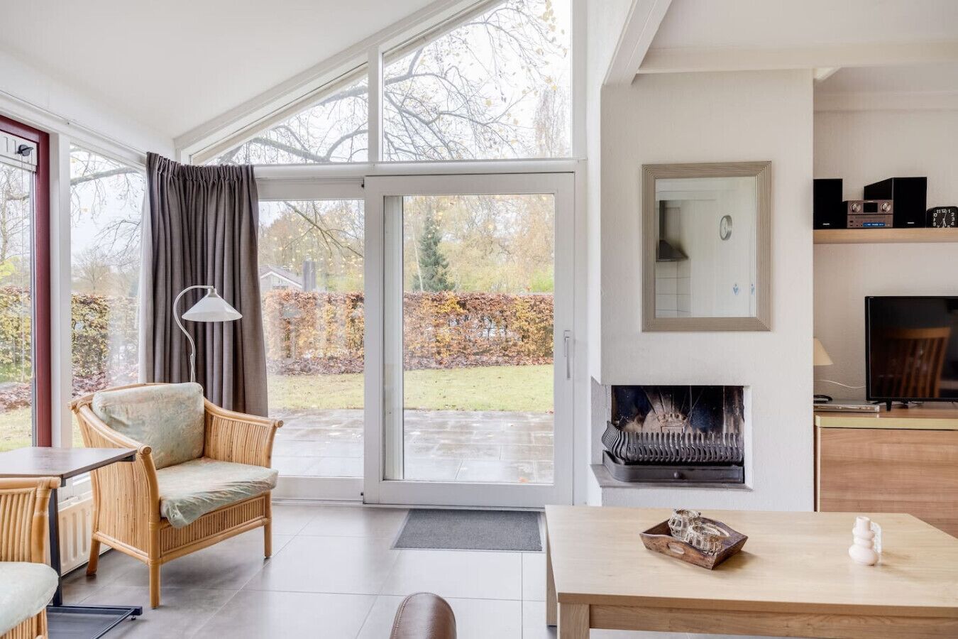 A modern living room with a large sliding glass door leading to a garden, a fireplace, and a television on a wooden stand.