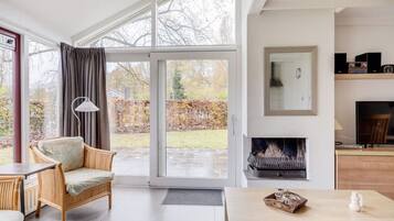A modern living room with a large sliding glass door leading to a garden, a fireplace, and a television on a wooden stand.