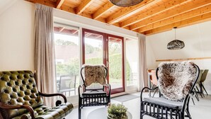 A modern interior with wooden beams, a leather armchair, two furry chairs, a dining table, and a potted plant. - ChiffChaff I Cottage Overlooking Spacious Garden (Zwiggelte)