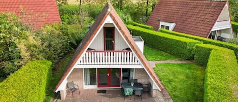 A triangular-roofed house with a balcony, surrounded by well-maintained hedges and a grassy lawn.