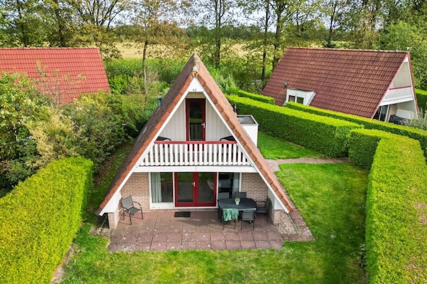 Et hus med et trekantet tag og balkon, omgivet af velplejede hække og en græsplæne.