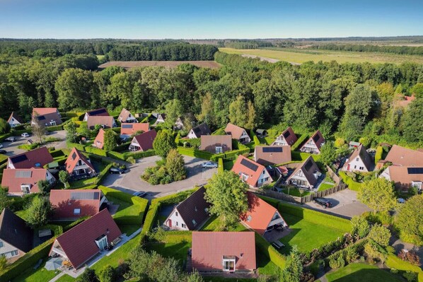 Luftaufnahme eines Wohngebiets mit Häusern, grünen Rasenflächen und einem bewaldeten Hintergrund.