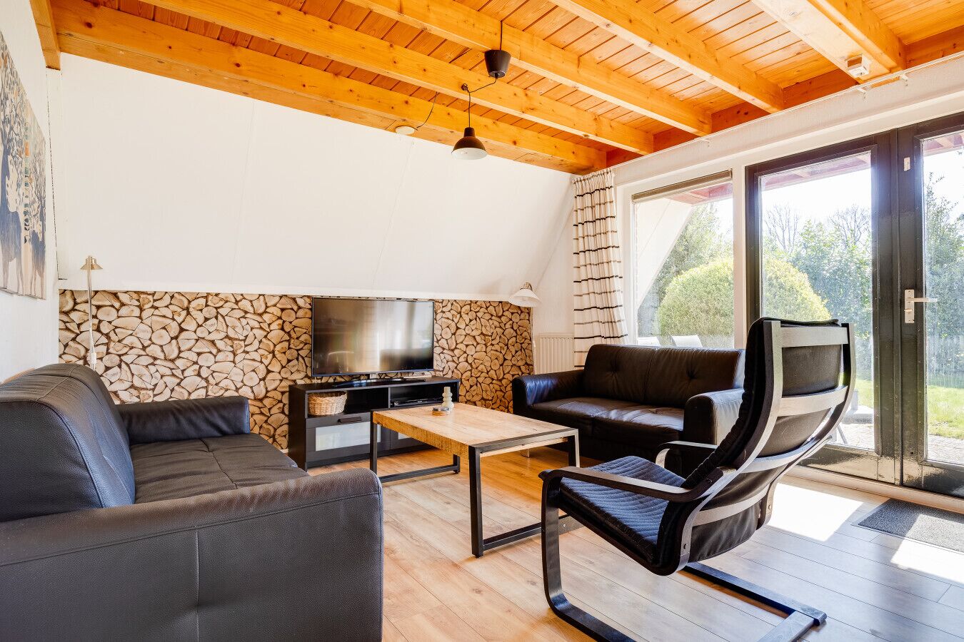 Ein modernes Wohnzimmer mit Steinwand, Flachbildfernseher, Ledersofa und Glastür zum Außenbereich.